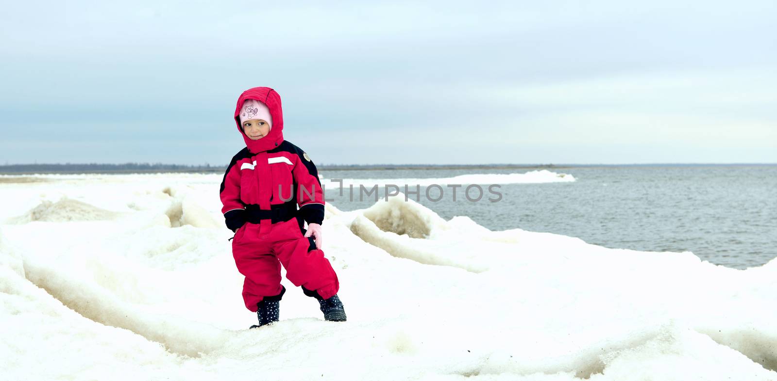 little girl in winter clothes on the snow-covered coast