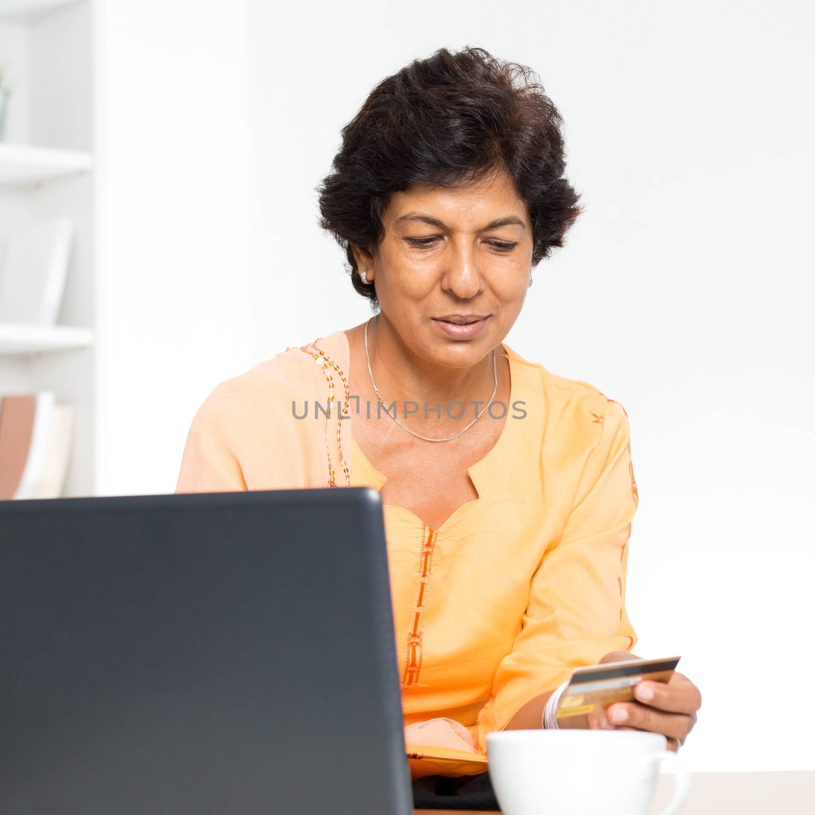 Old people and modern technology concept. Portrait of a 50s Indian mature woman hand holding credit card, using online internet payment at home. Indoor senior people living lifestyle.