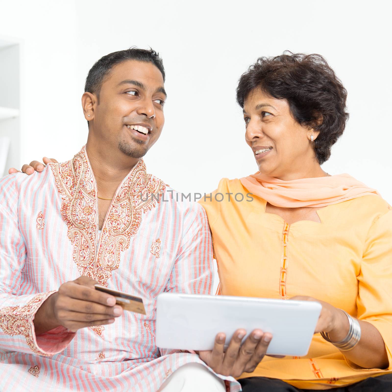 Portrait of Indian family using internet payment at home. Mature 50s Indian woman and 30s grown son happy online shopping with credit card.