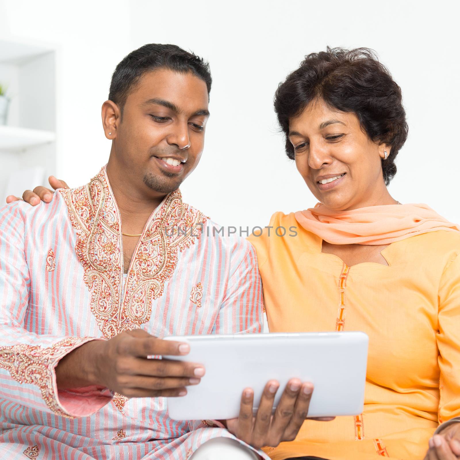 Portrait of Indian family using social media at home. Mature 50s Indian woman and son looking at tablet computer.
