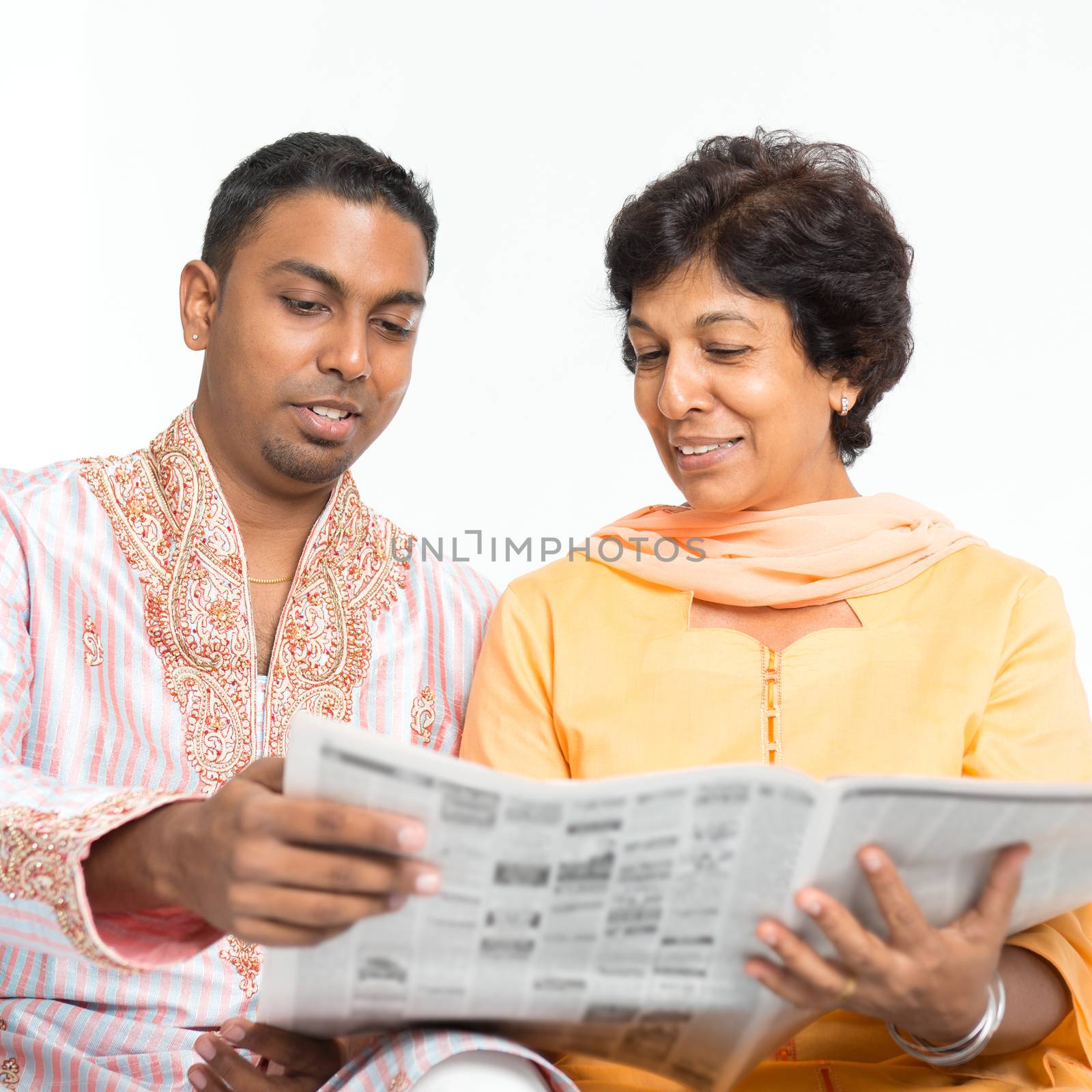 Portrait of Indian family reading newspaper together at home. Mature 50s Indian mother and 30s grown son.