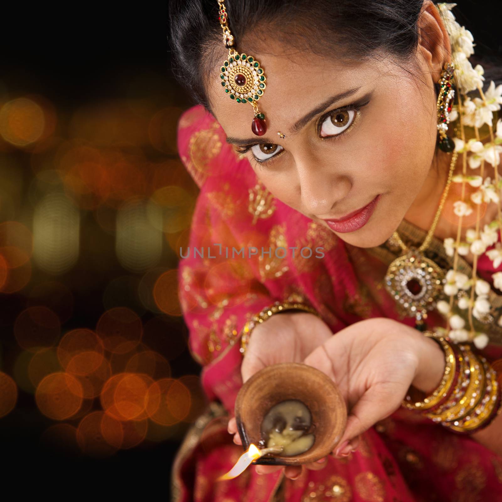 Indian female in traditional sari lighting oil lamp and celebrating Diwali or deepavali, fesitval of lights at temple. Girl hands holding oil lamp, beautiful lights bokeh background.