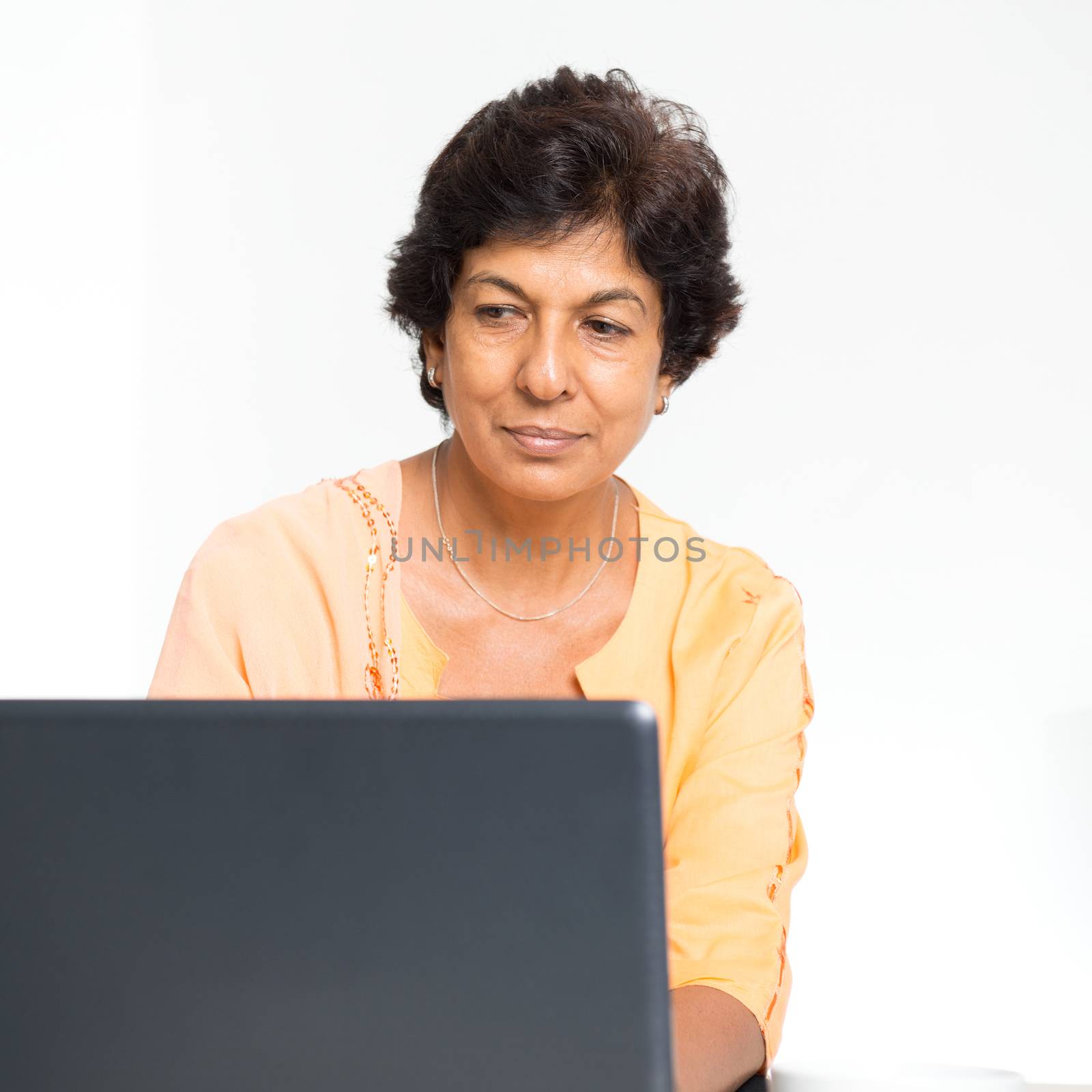 Older people and modern technology concept. Portrait of a 50s Indian mature woman using laptop computer at home. Indoor senior people living lifestyle.
