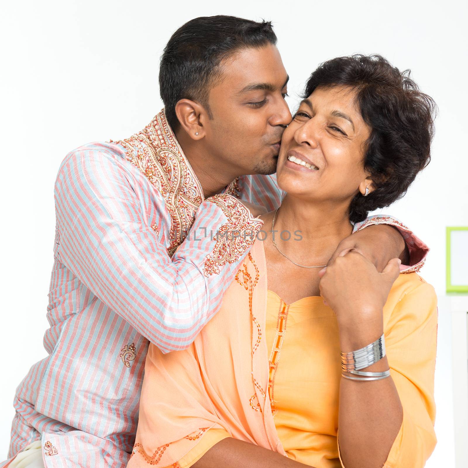 Portrait of happy Indian family at home. Indian 30s grown son kissing his mature 50s mother.