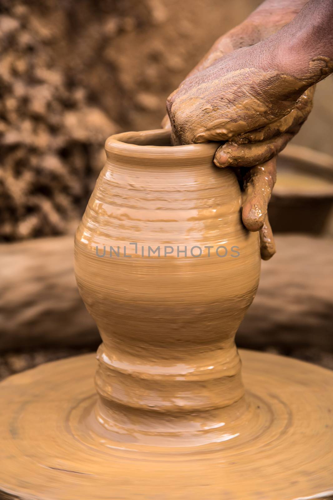 Vertical image of the hands of a potter creating earthen pots from soft clay
