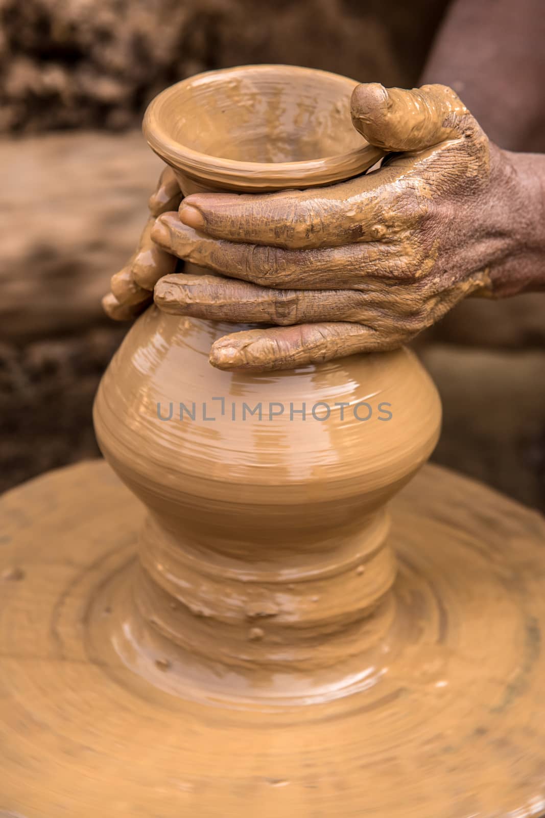 Hands of a clay artisan working to make a flower vase out of soft clay on a rotating cart wheel