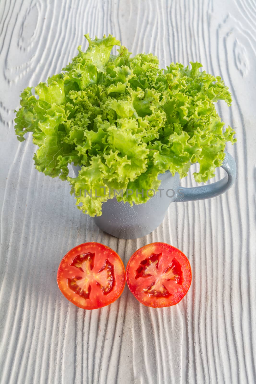 garnich lettuce in a grey mug, half cut tomato on wooden background