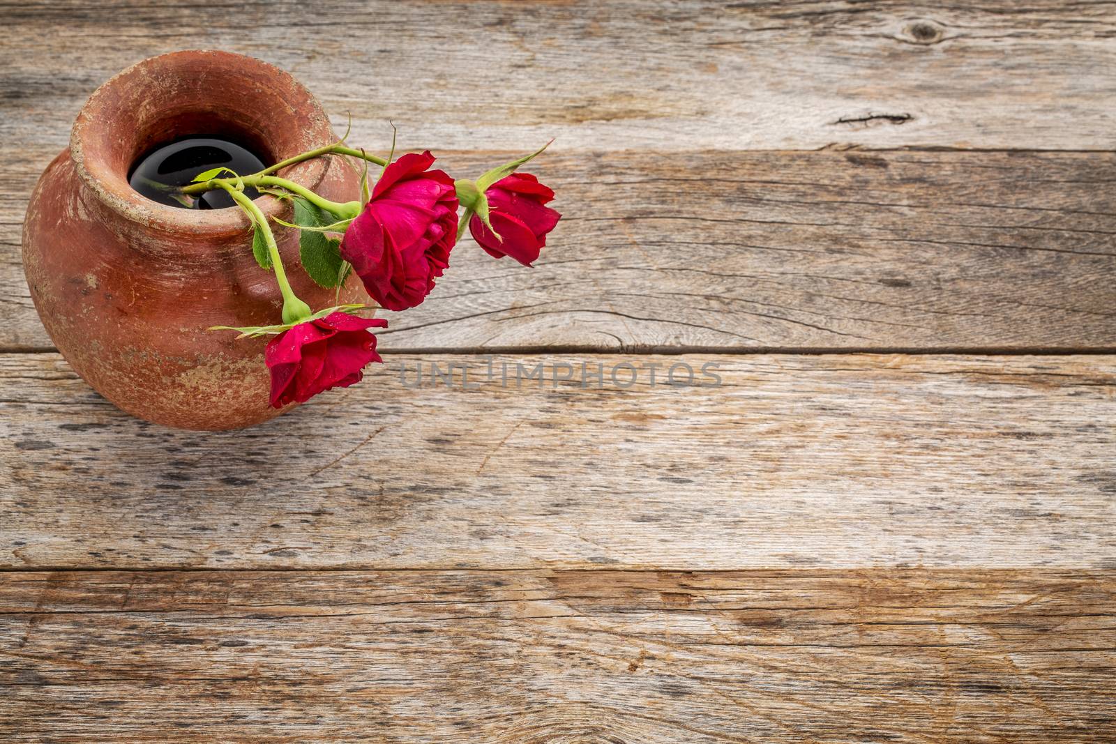 red roses in a a clay vase against rustic weathered wood with a copy space