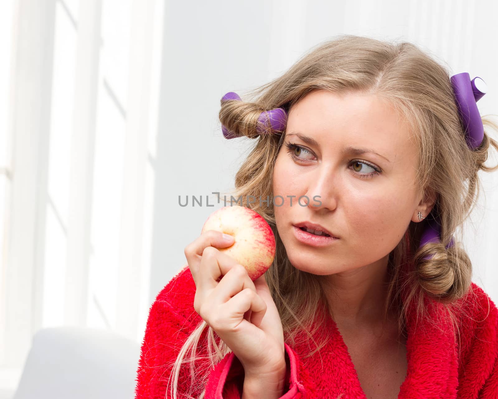 Girl in a red robe and curlers eating an apple