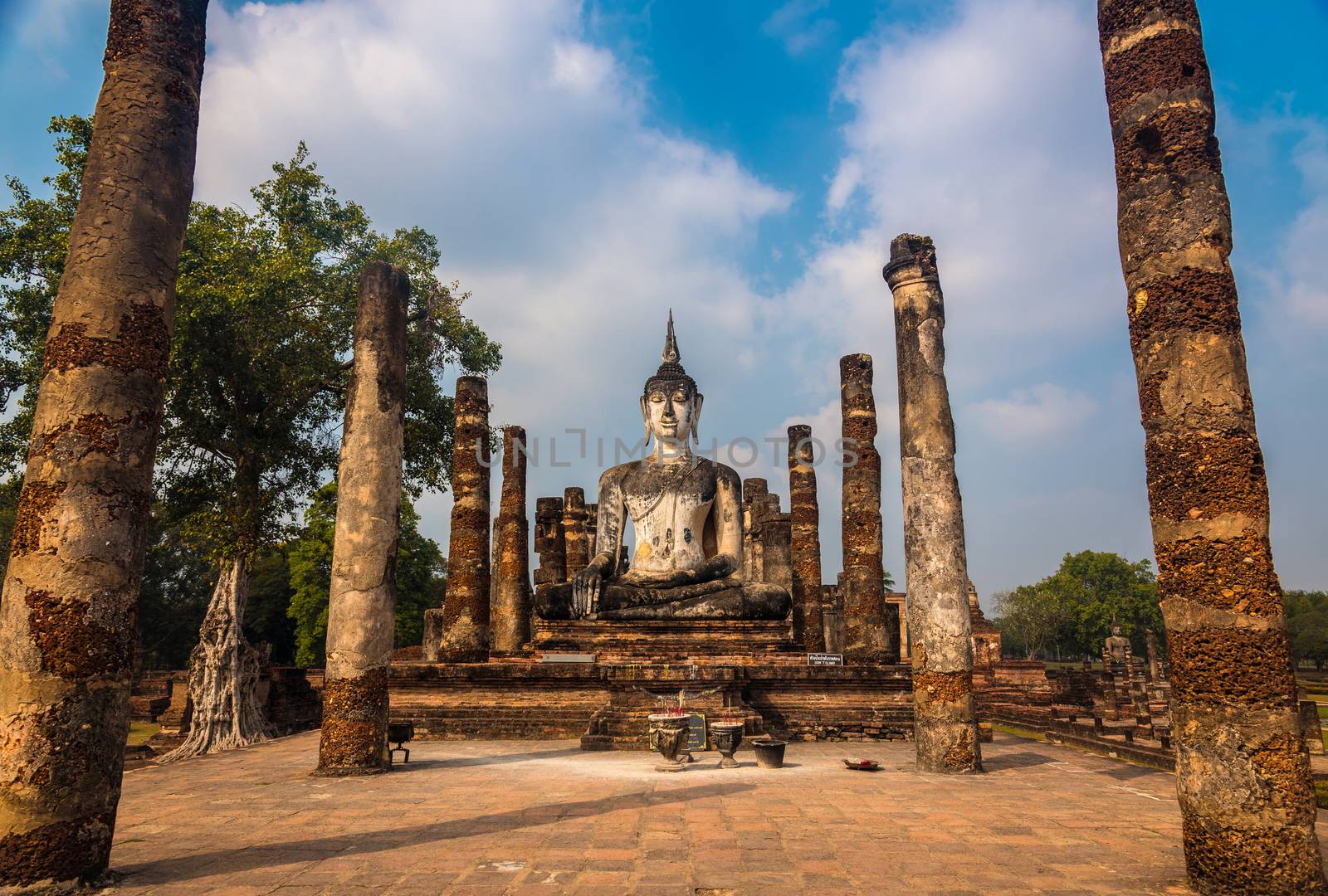 Ancient Buddha statue surrounded by the ruins of old pagoda in Wat Mahathat in Sukhothai, Thailand