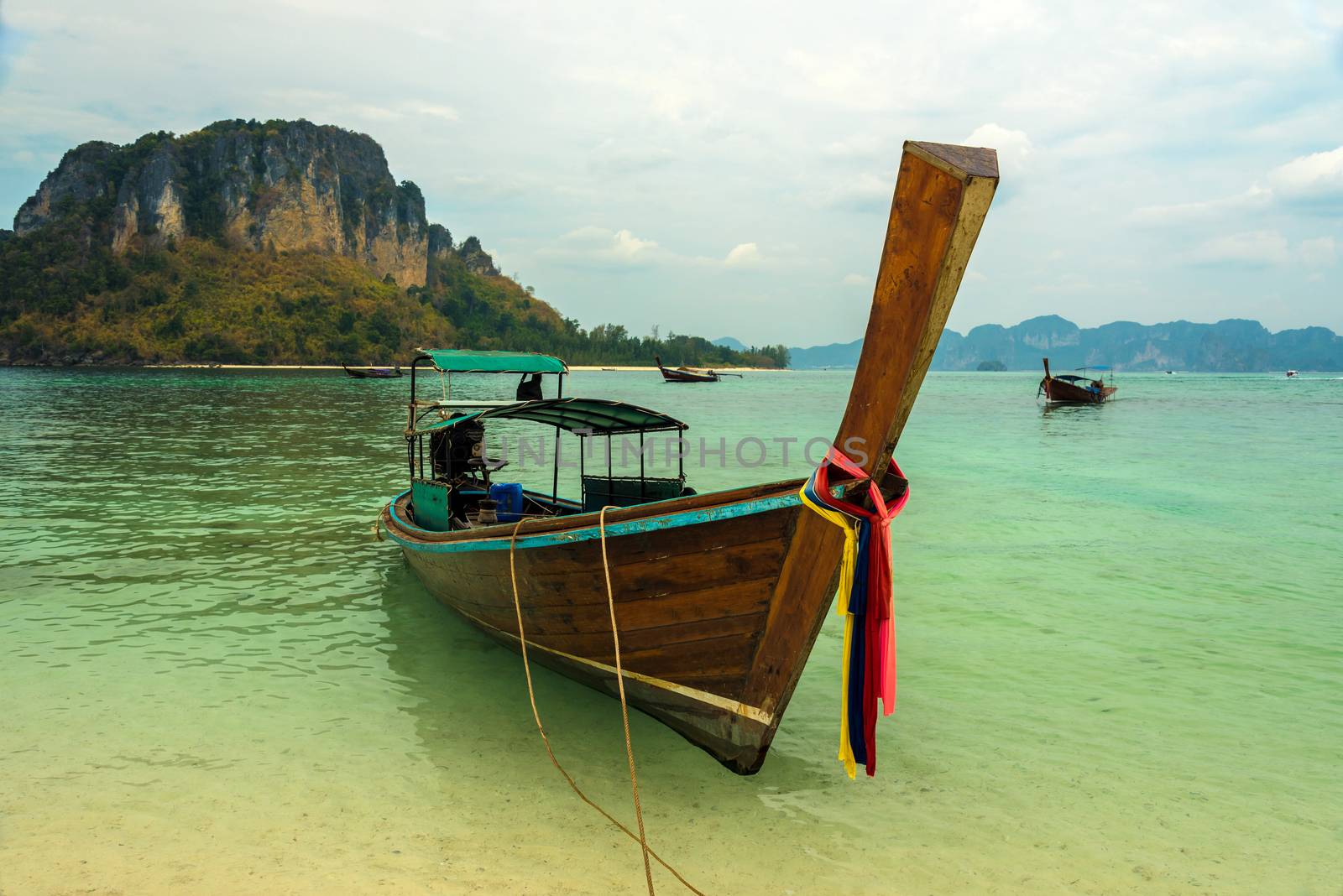 Longtail boat moored off a white sand Krabi beach in the crystal clear turquoise waters of Andaman sea.