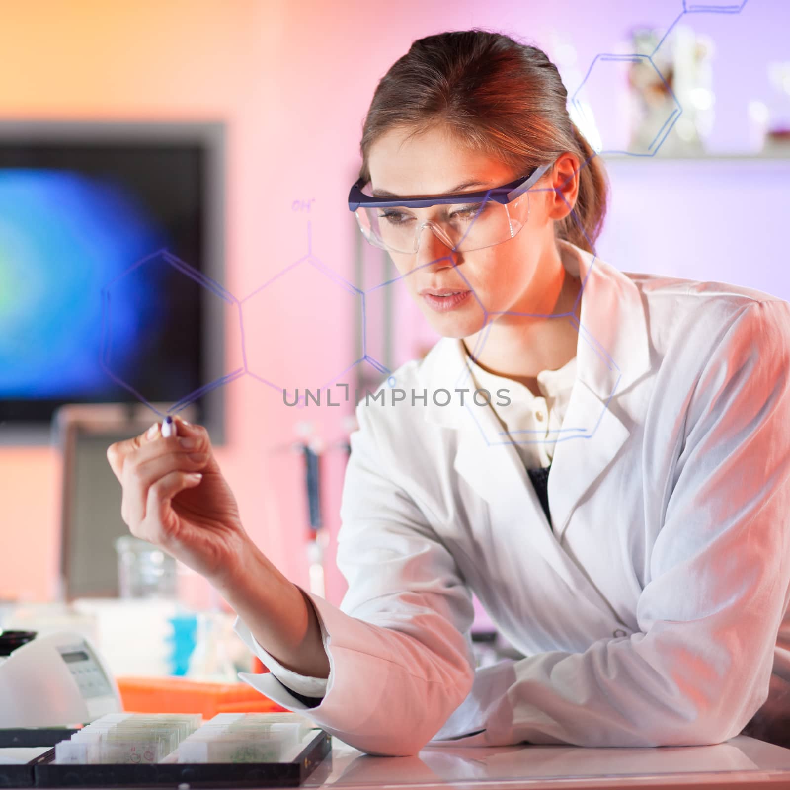 Life science researcher working in laboratory. Portrait of a confident female health care professional in his working environment writing structural chemical formula on a glass board.