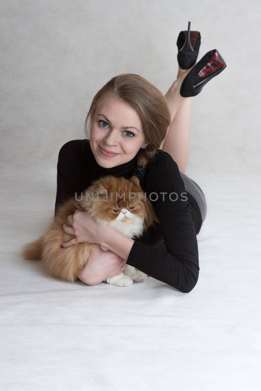 Very nice blonde lies on a floor and holds a red persian kitten