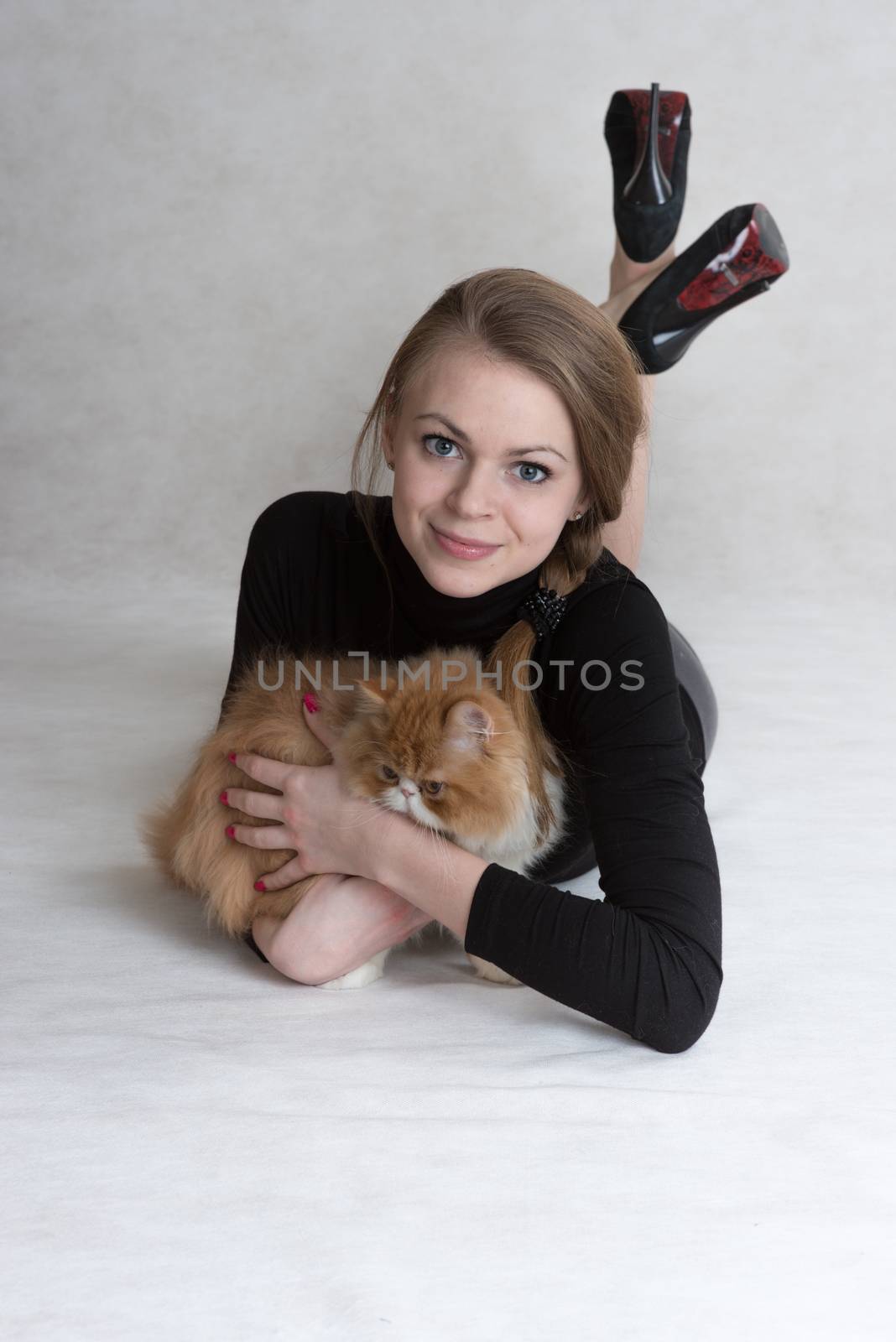 Very nice blonde lies on a floor and holds a red persian kitten