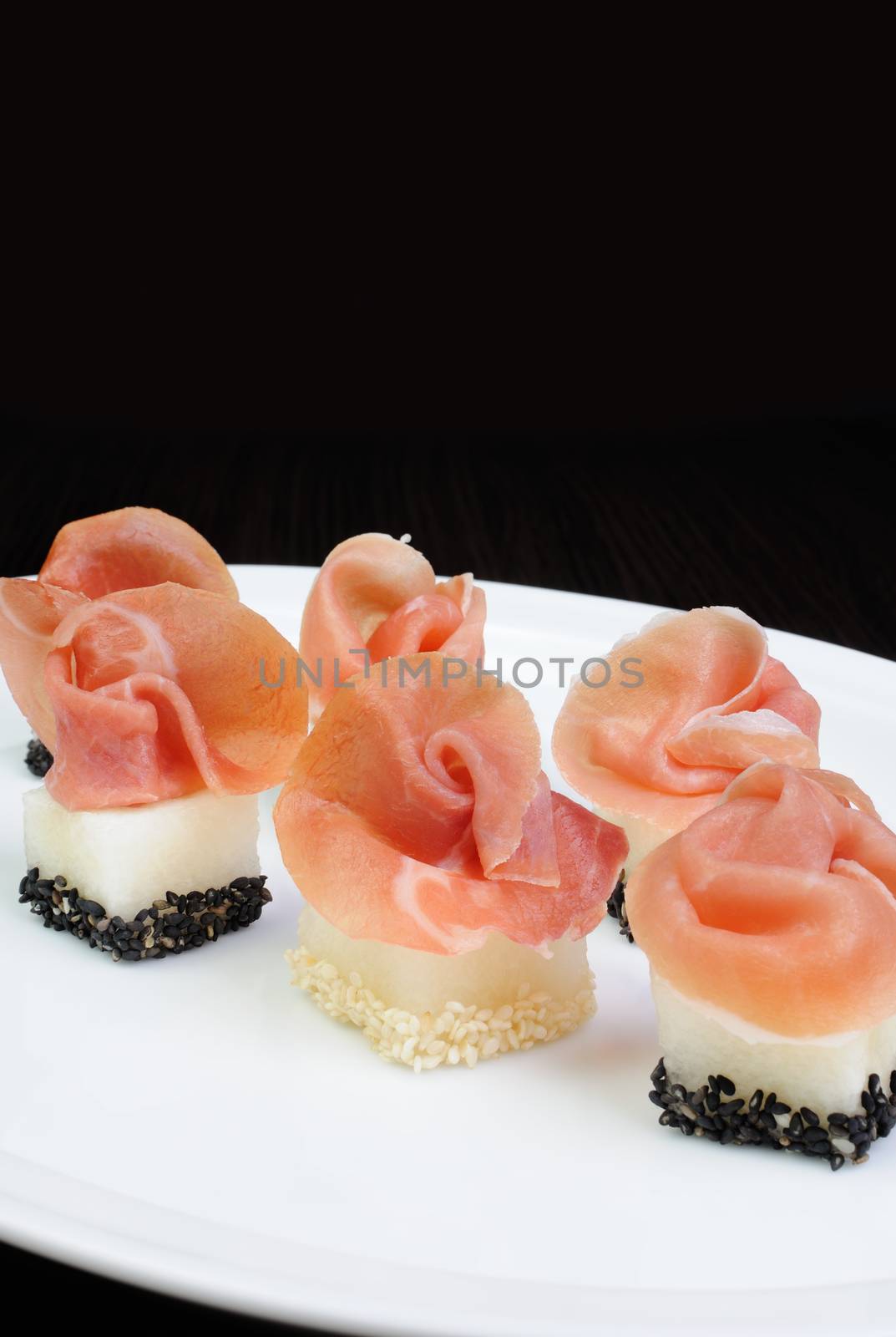 Appetizer of melon cubes in sesame with a slice of gammon