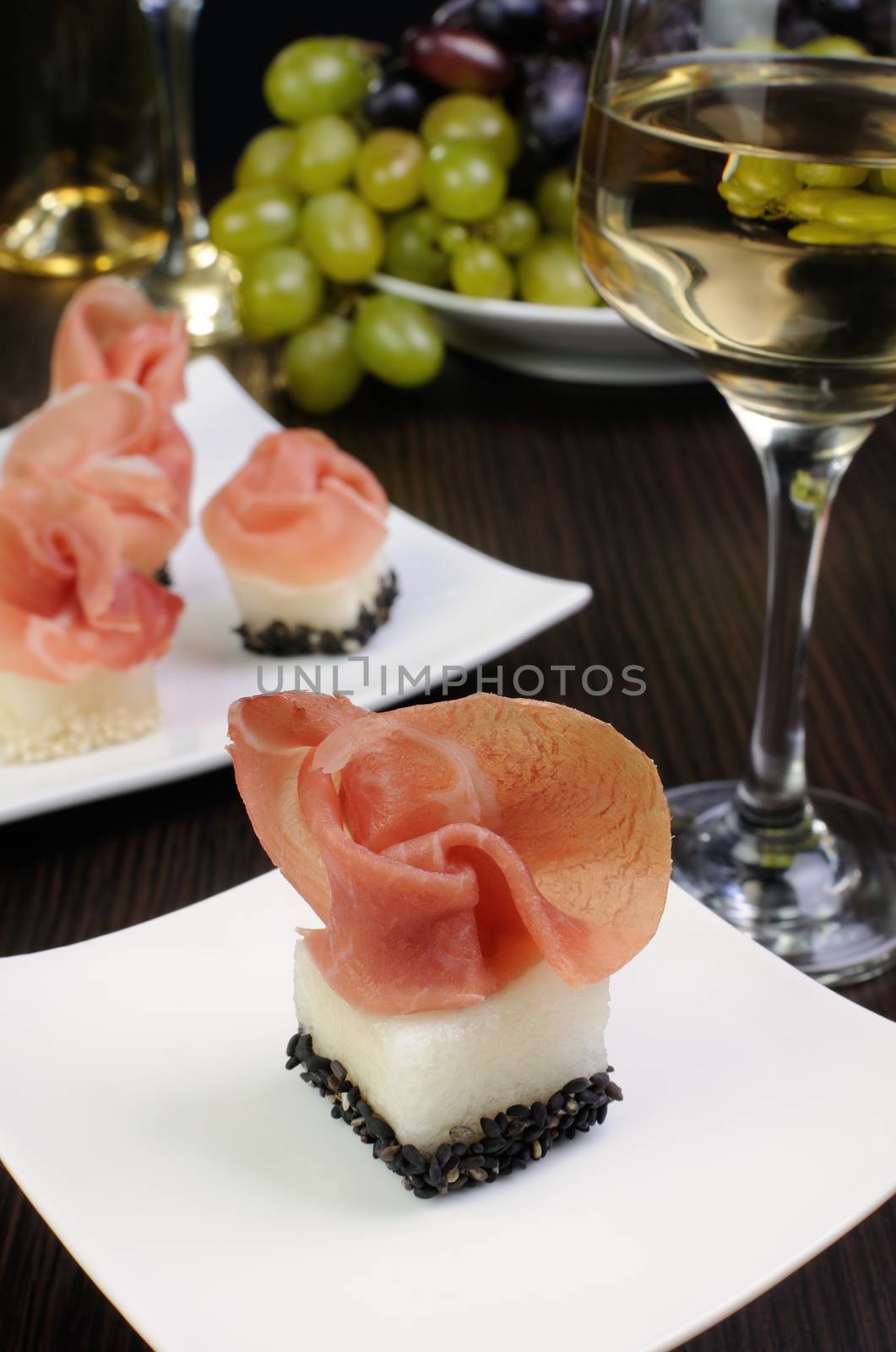 Appetizer of melon cubes in sesame with a slice of gammon