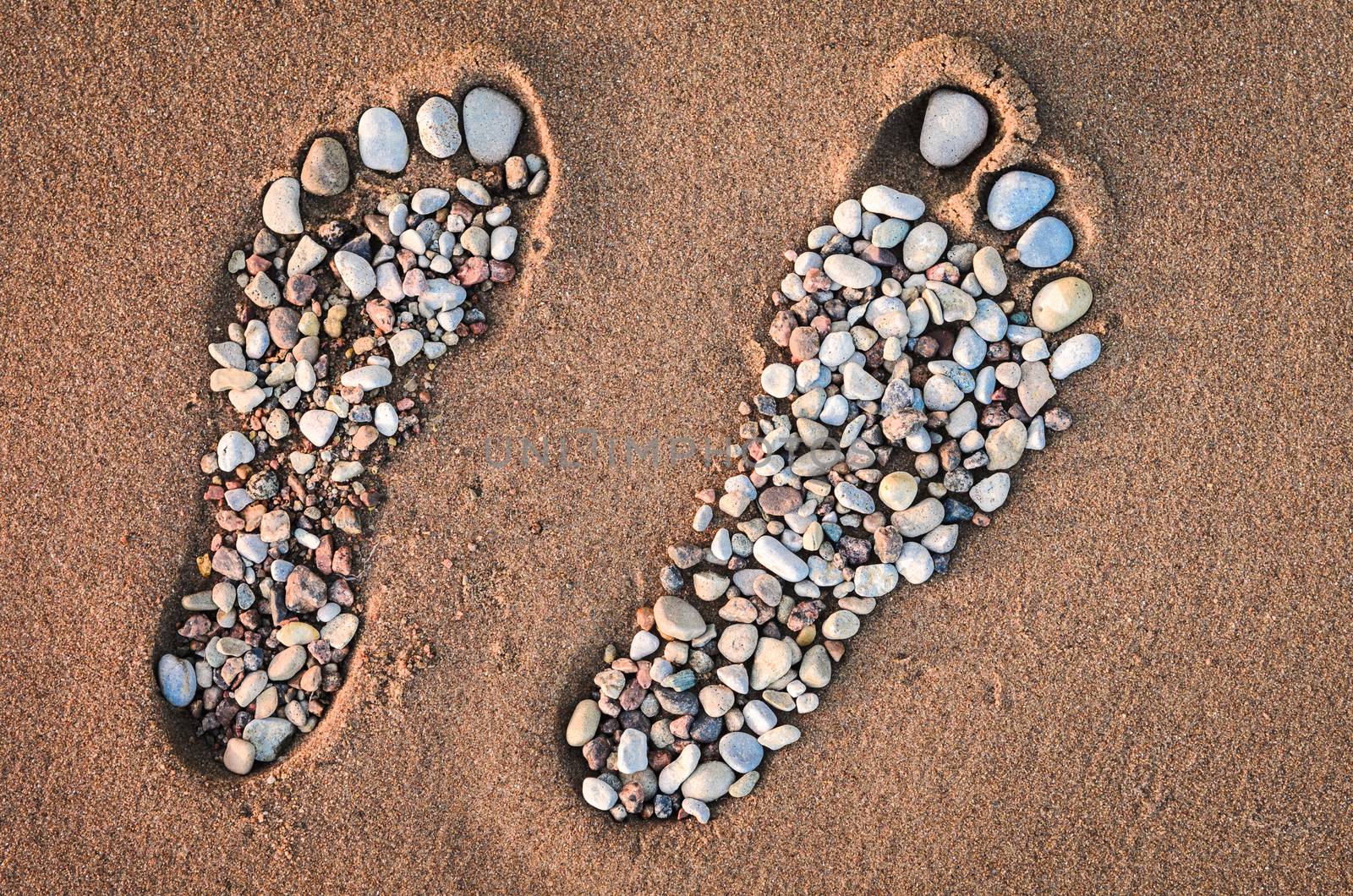 Bare feet made of pebble on the sandy beach