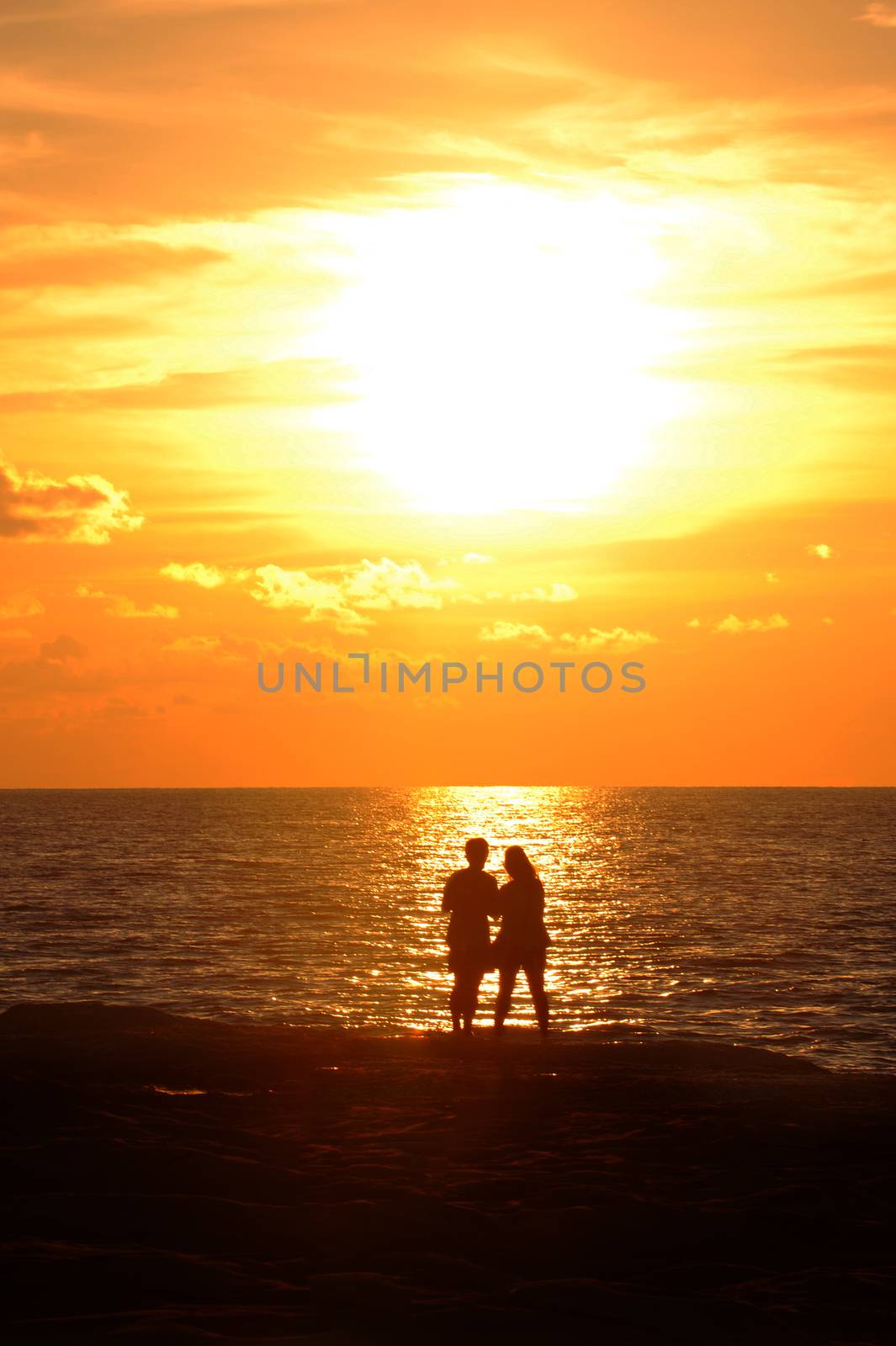 Young couple standing on the shore and looks at the setting sun by the sea
