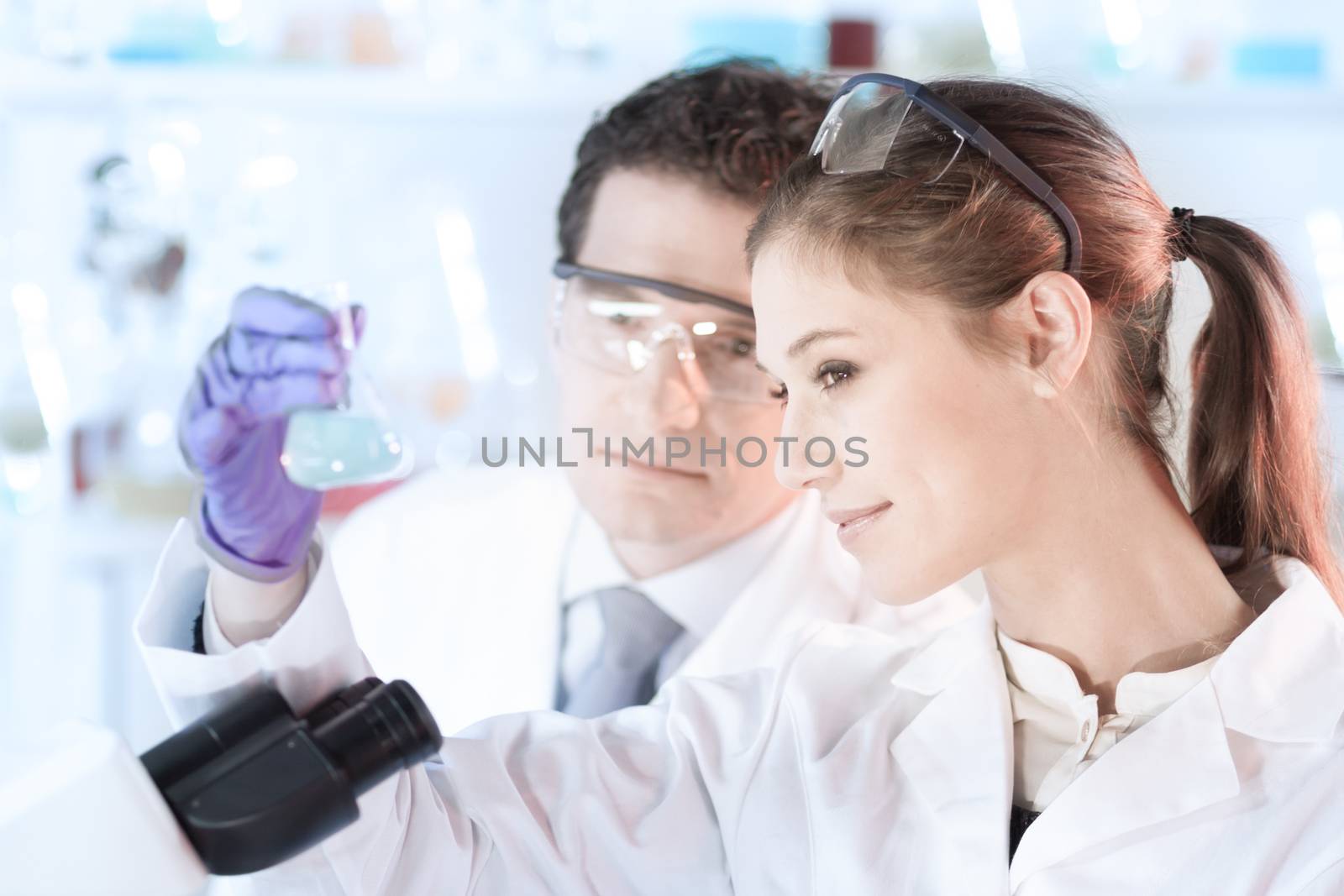 Life scientist researching in laboratory. Attractive young scientist and her post doctoral supervisor looking at the microscope slide in the forensic laboratory. Healthcare and biotechnology.