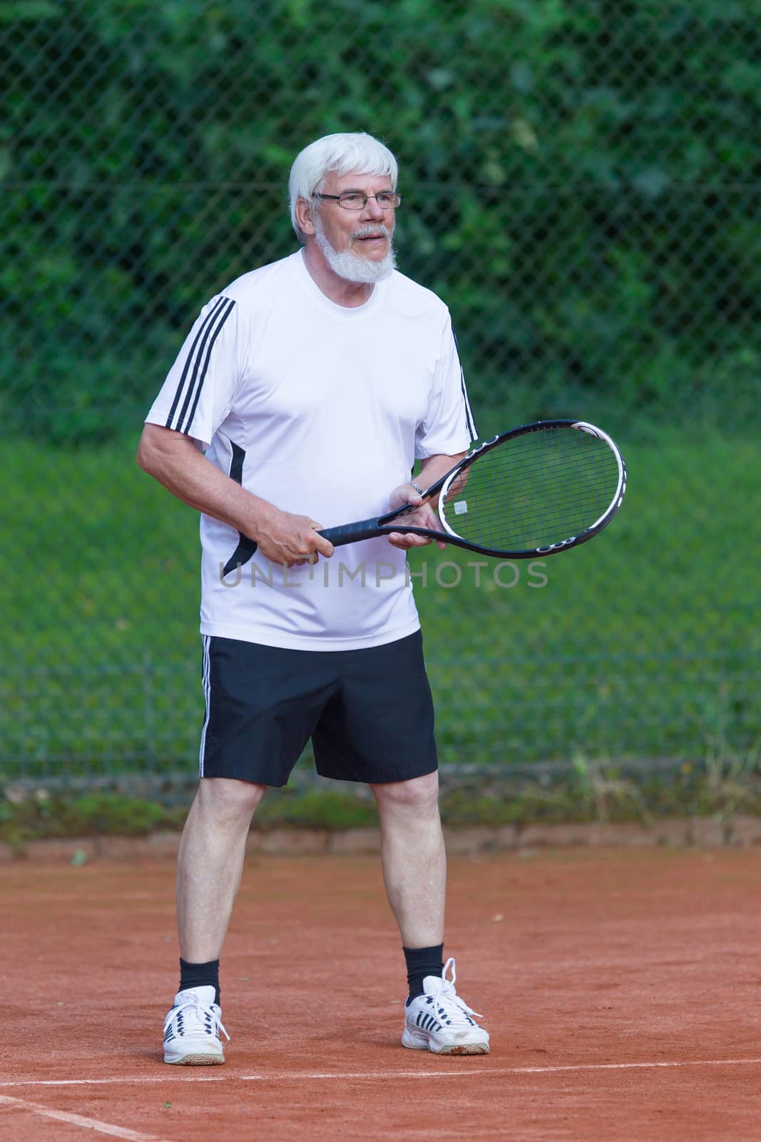 Senior man playing tennis on a gravel court