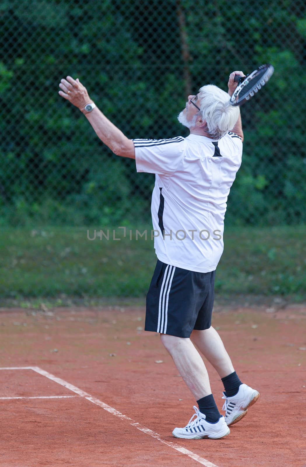 Senior man playing tennis on a gravel court