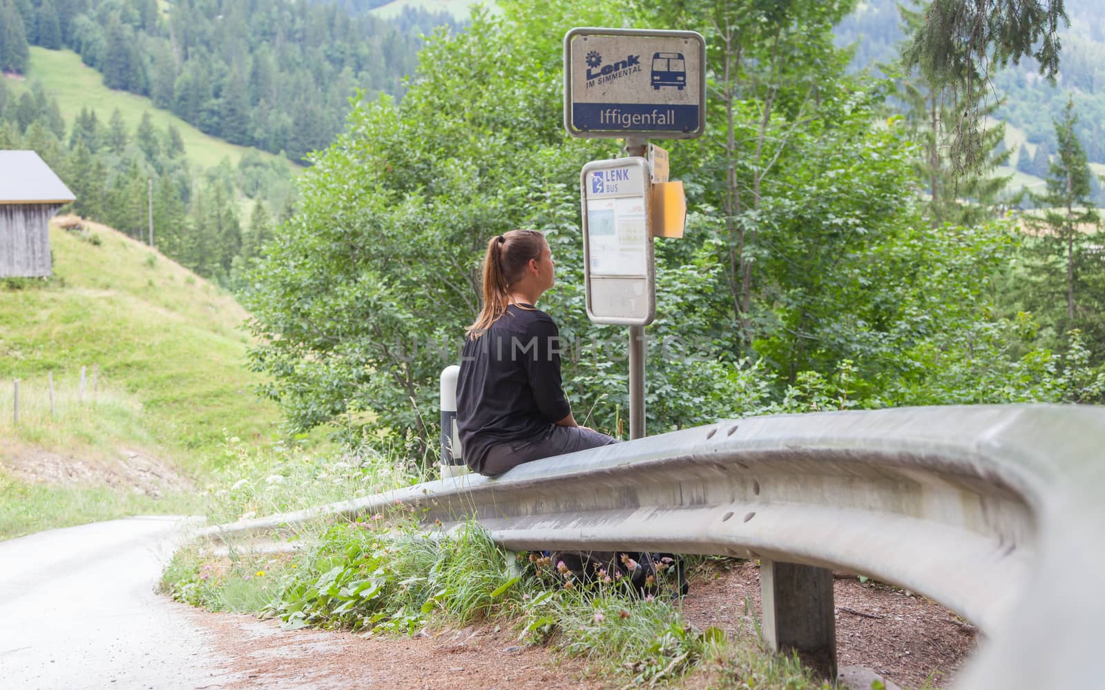 LENK, SWITZERLAND - JULY 23, 2015: Young woman checking the timetable at the bus stop in Lenk, Switzerland on July 23, 2015.