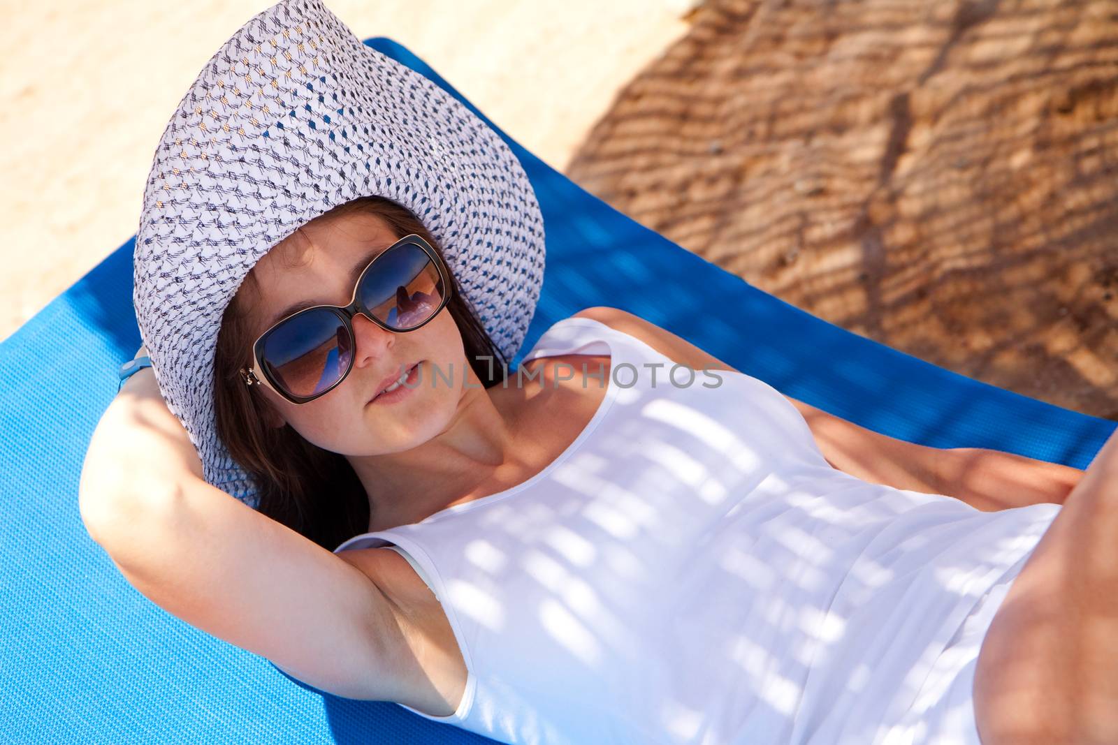 Young woman relaxes on a lounger on the beach under umbrella
