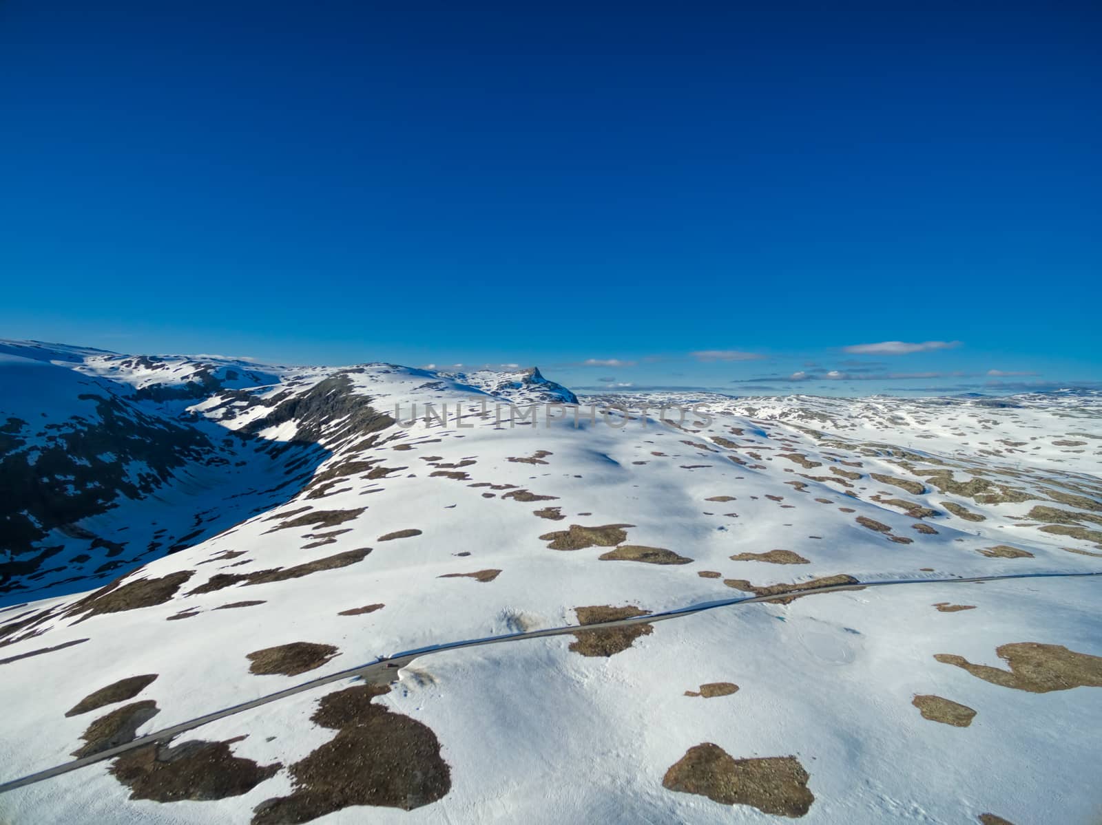 Aerial view of narrow road in snowy landscape of mountain pass Aurlandsfjellet in Norway on sunny day