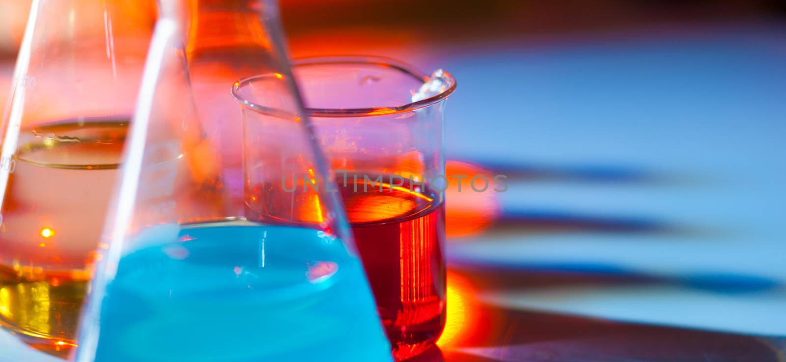 Backlit laboratory test flask containing colorful liquids. Panoramic composition.