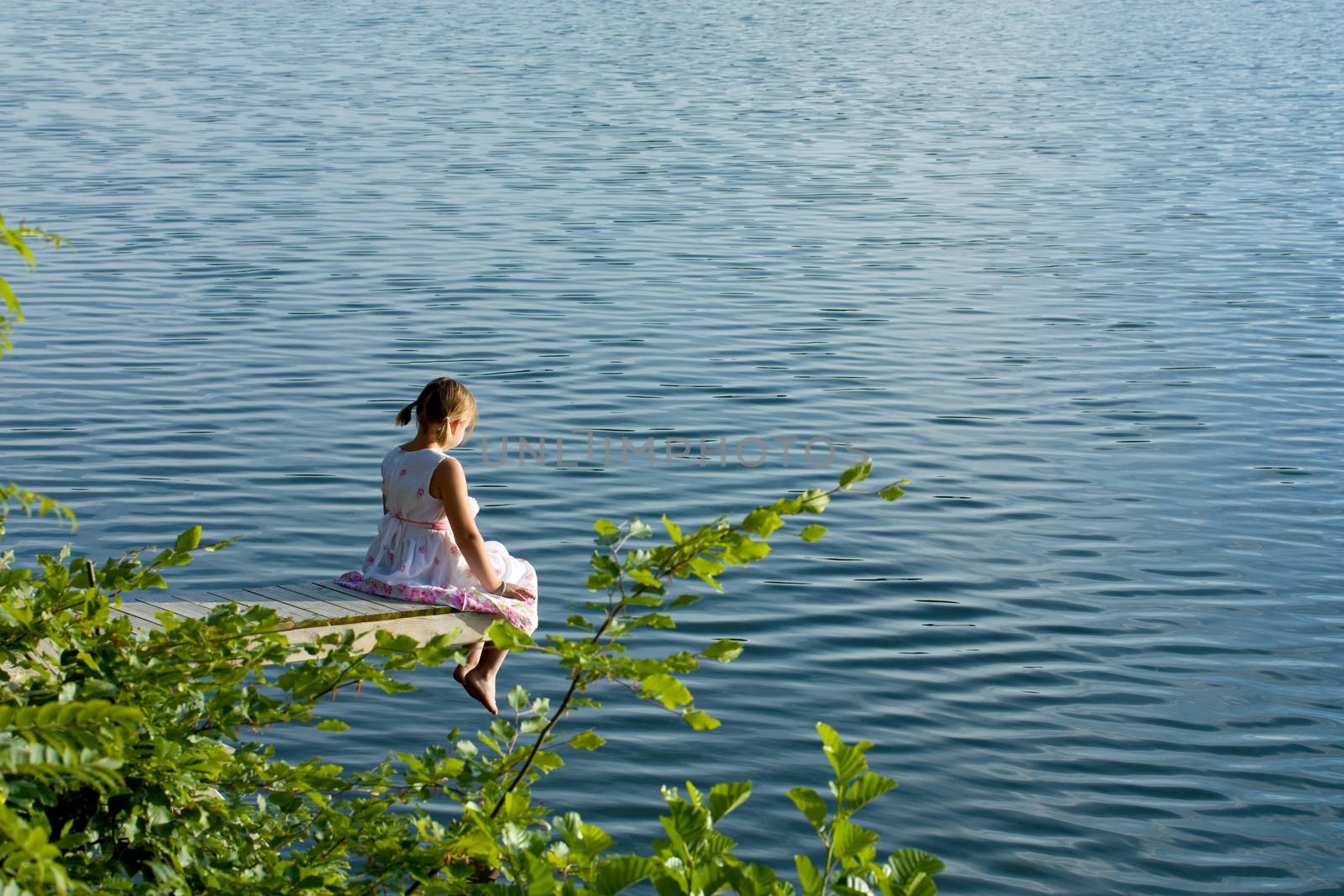 Girl in summer dress sitting at deck over water by kavring