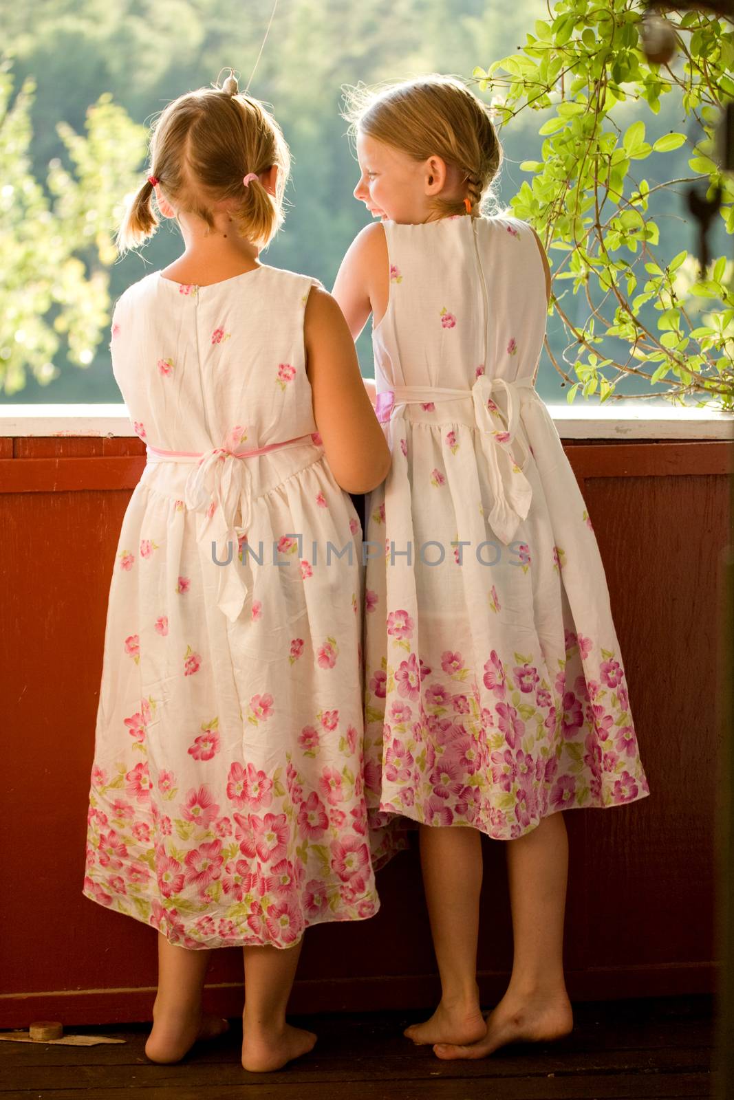 Twin girls in summer dresses on porch laughing
