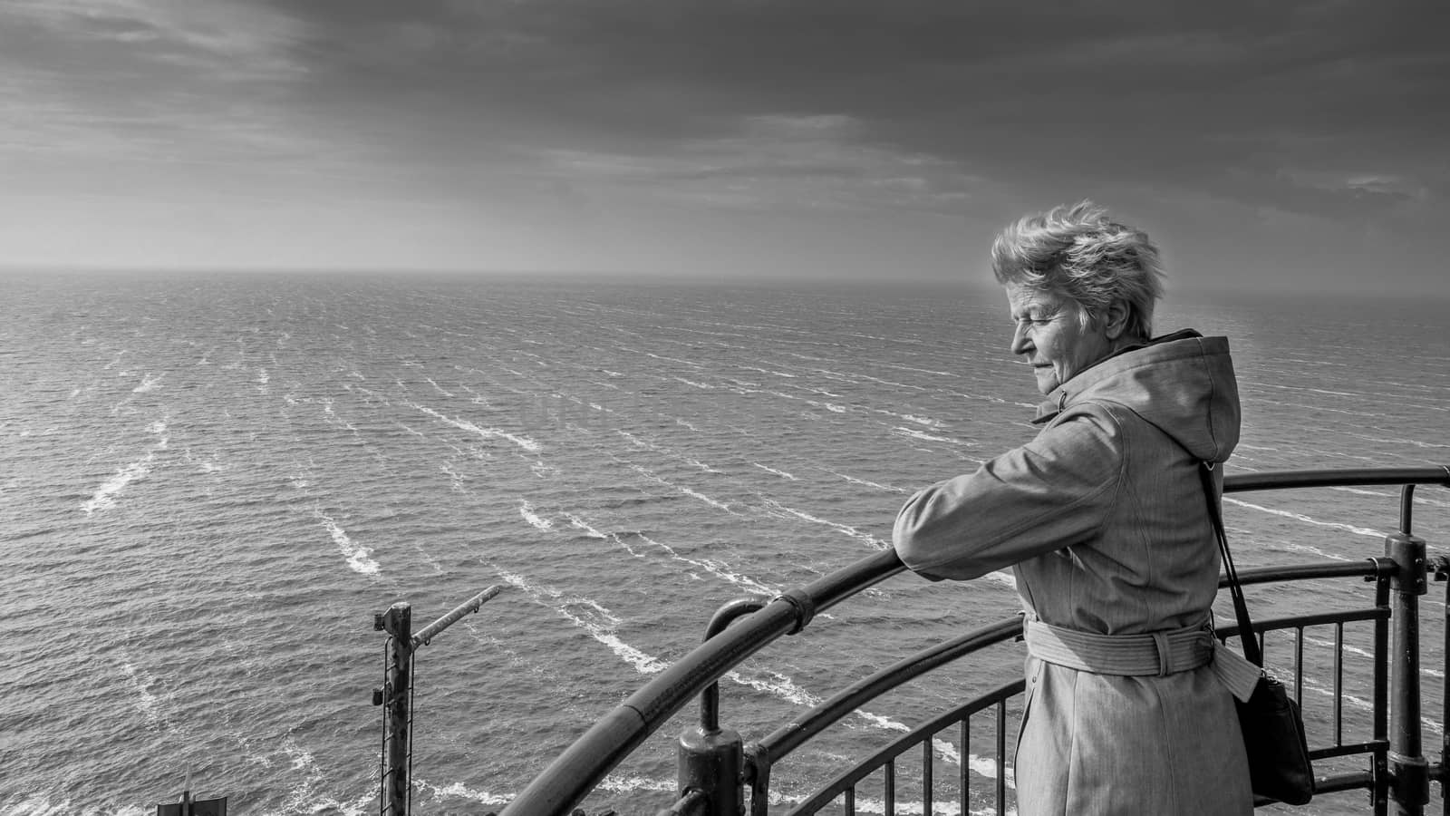 Senior Woman looking at the Storm over the IJselmeer from the lighthouse in the historic fishing village of Urk in the Netherlands in a black and white photo