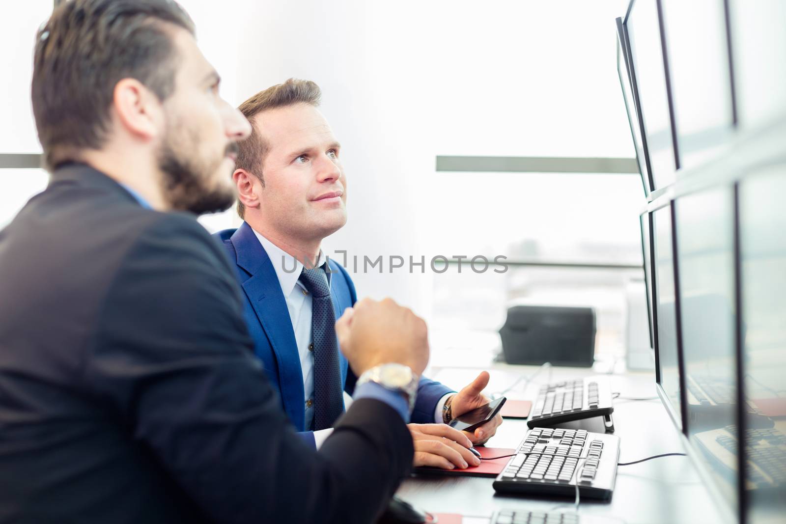 Successful businessmen trading stocks. Stock traders looking at graphs, indexes and numbers on multiple computer screens. Colleagues in traders office. Business success. 