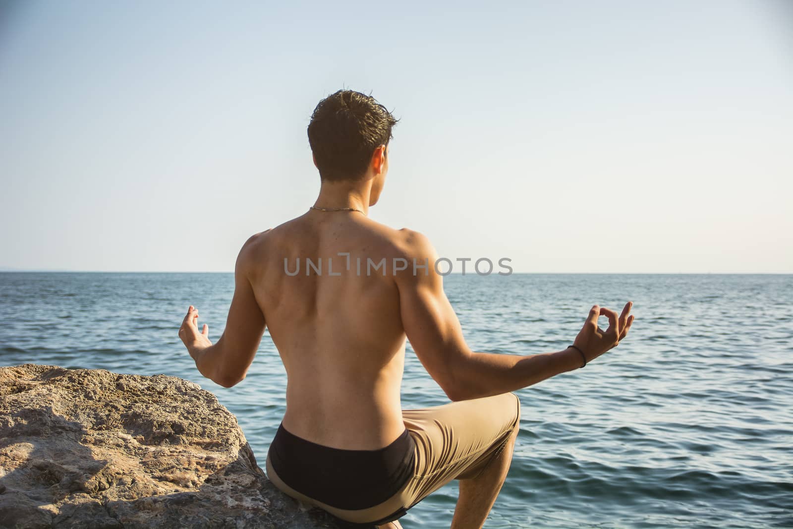 Young Man Meditating or Doing Yoga Exercise by Sea by artofphoto