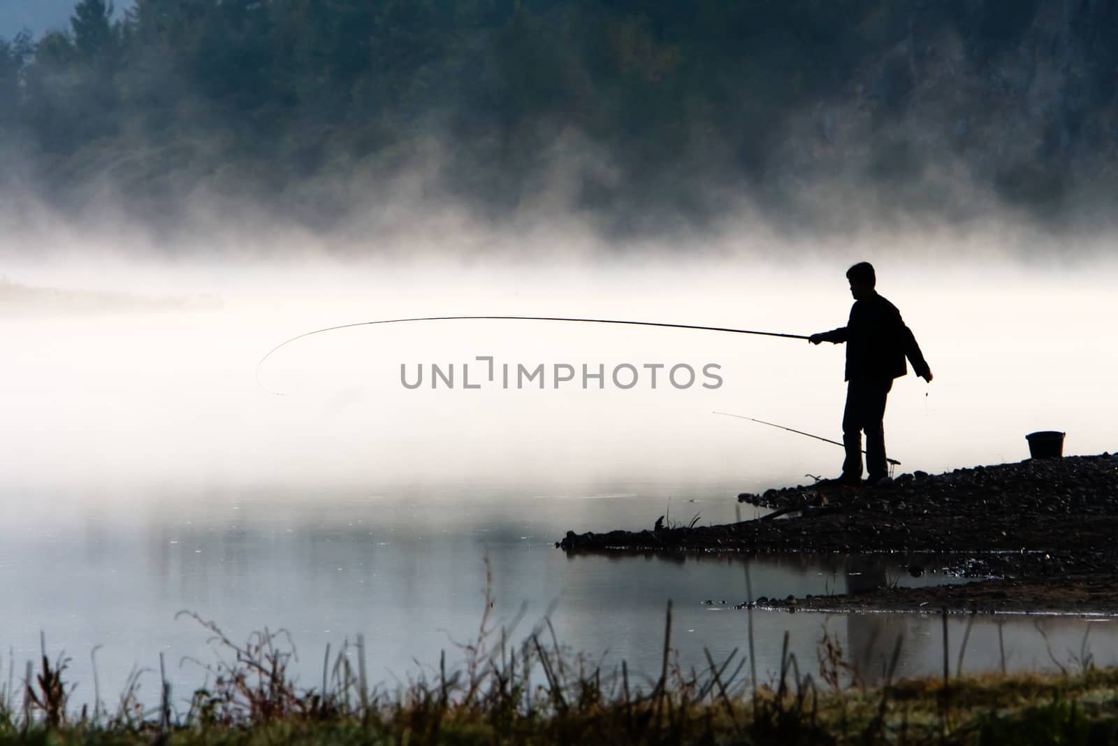 Man fishing at river shore in the morning.