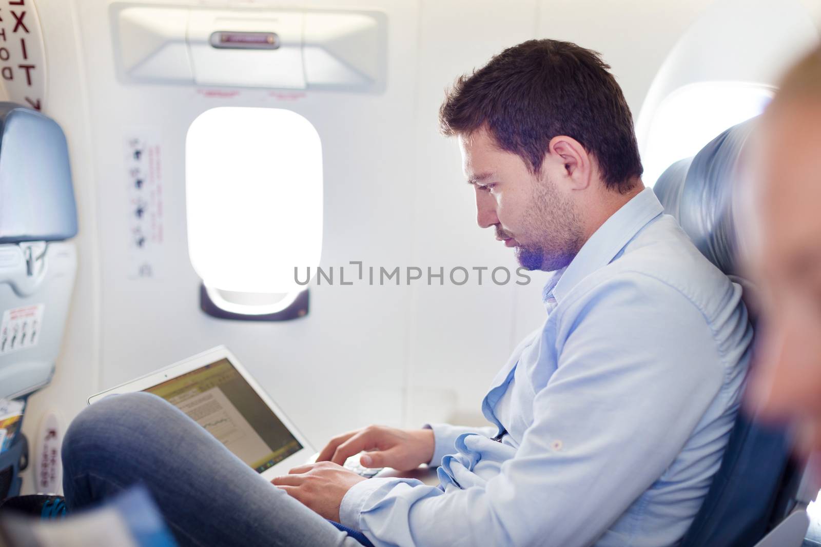 Casually dressed middle aged man working on laptop in aircraft cabin during his business travel. Shallow depth of field photo with focus on businessman eye.