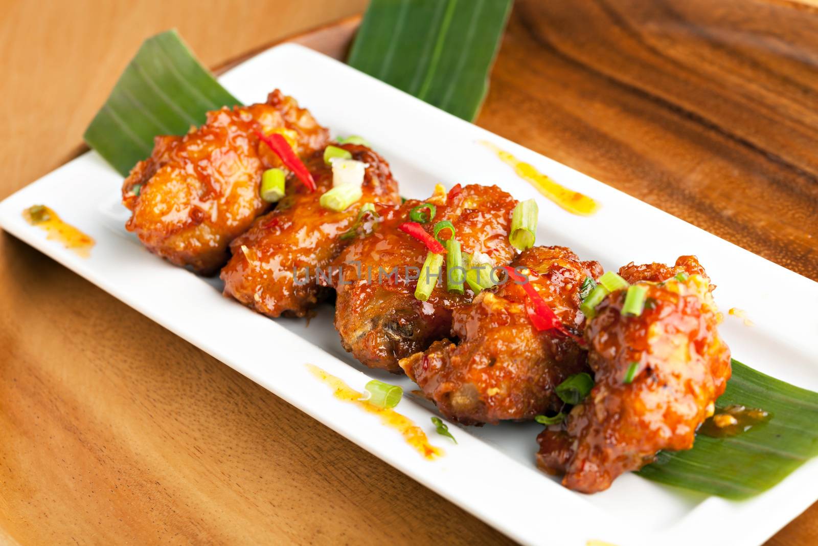 Thai style spicy chicken wings appetizer on a contemporary white plate.