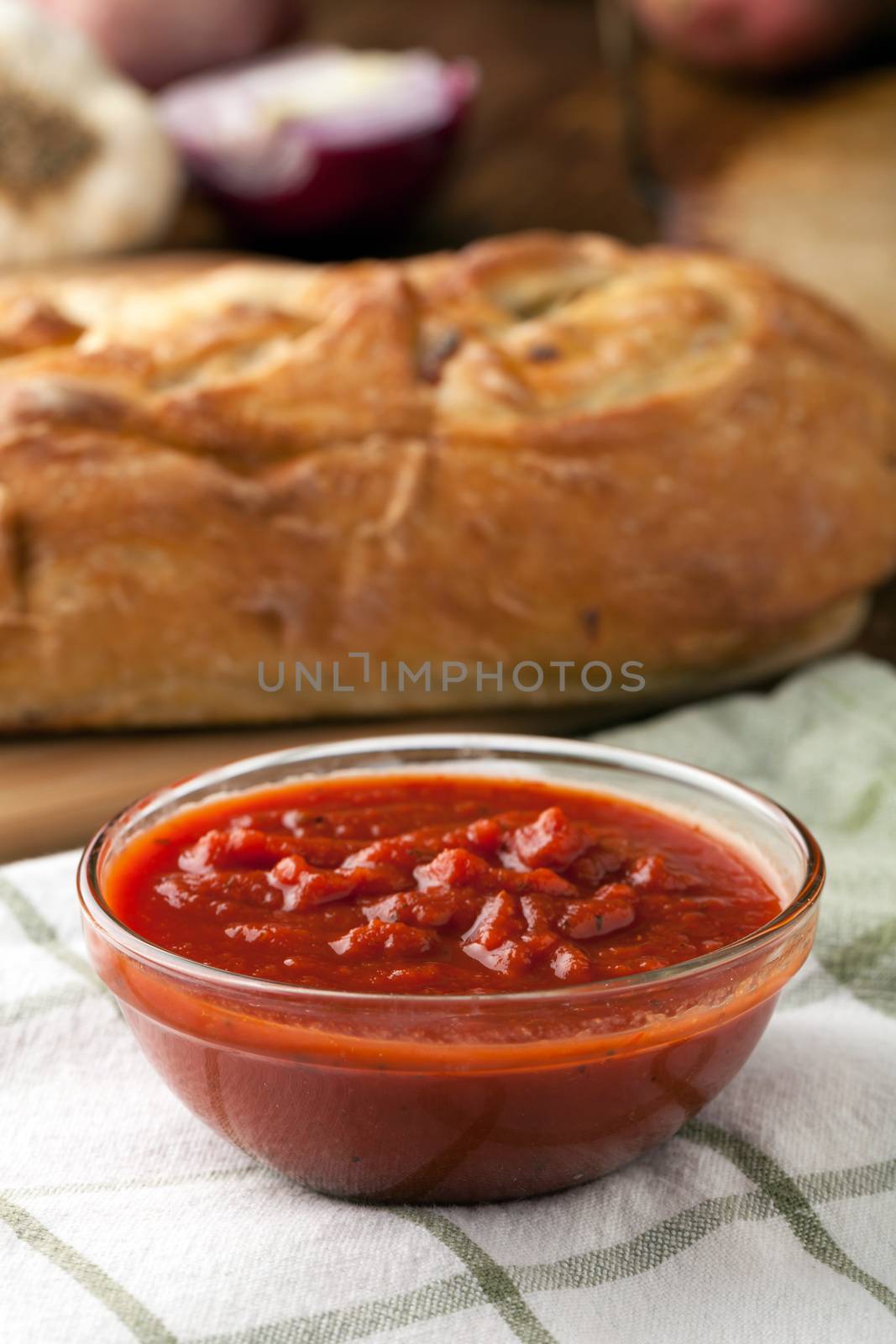 Freshly prepared pasta or pizza sauce marinara in a glass bowl. Bread in background.