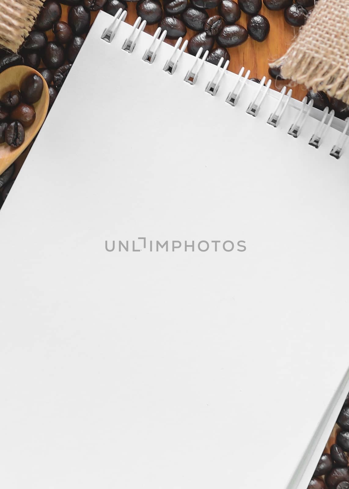 White notebook for your text with sackcloth and coffee beans on wooden spoon.