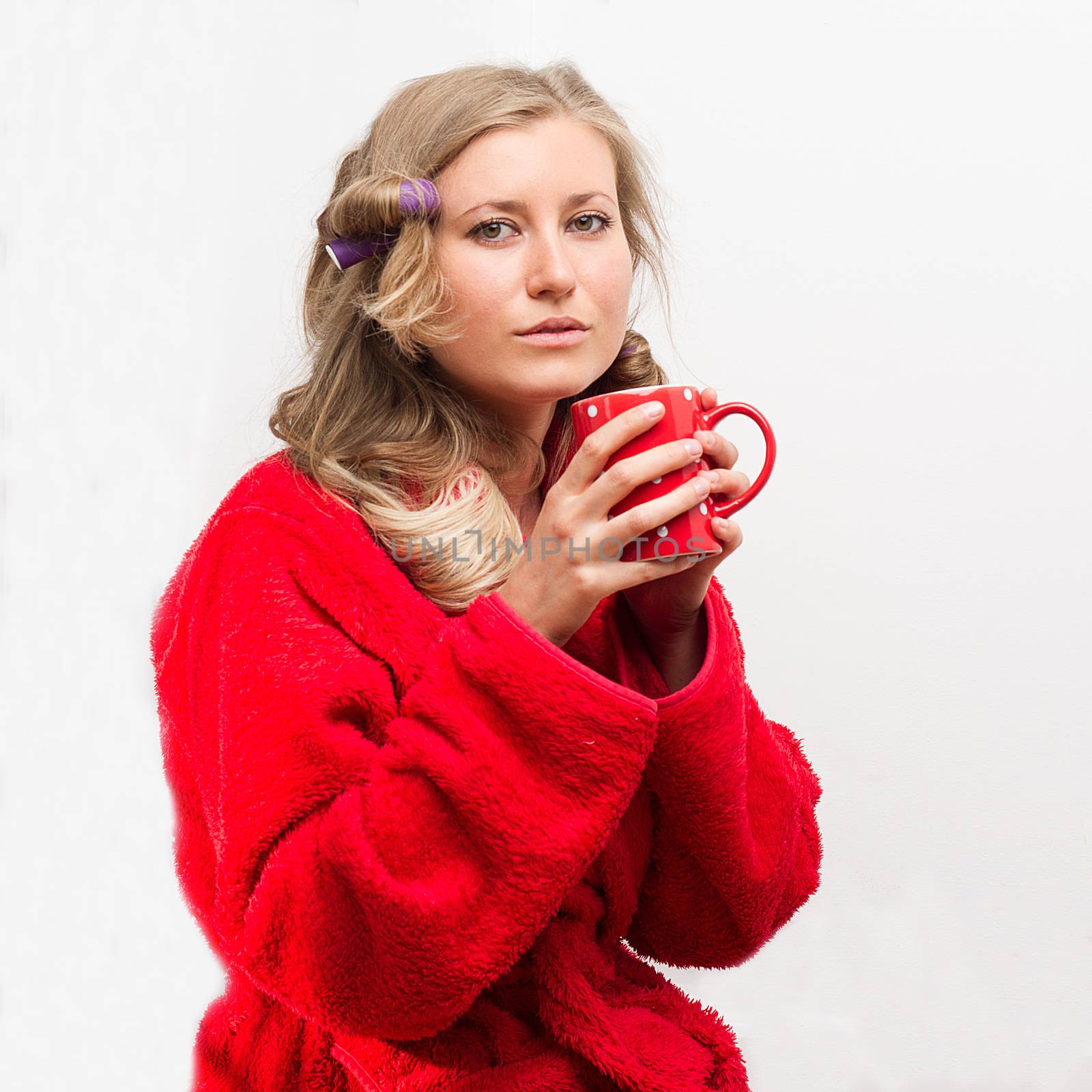 Half-length portrait of pretty young housewife wearing curlers and  wrapper holding red cup of tea having a rest