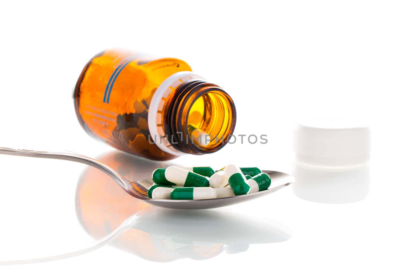 Tablets on a spoon with a brown bottle, on a white background