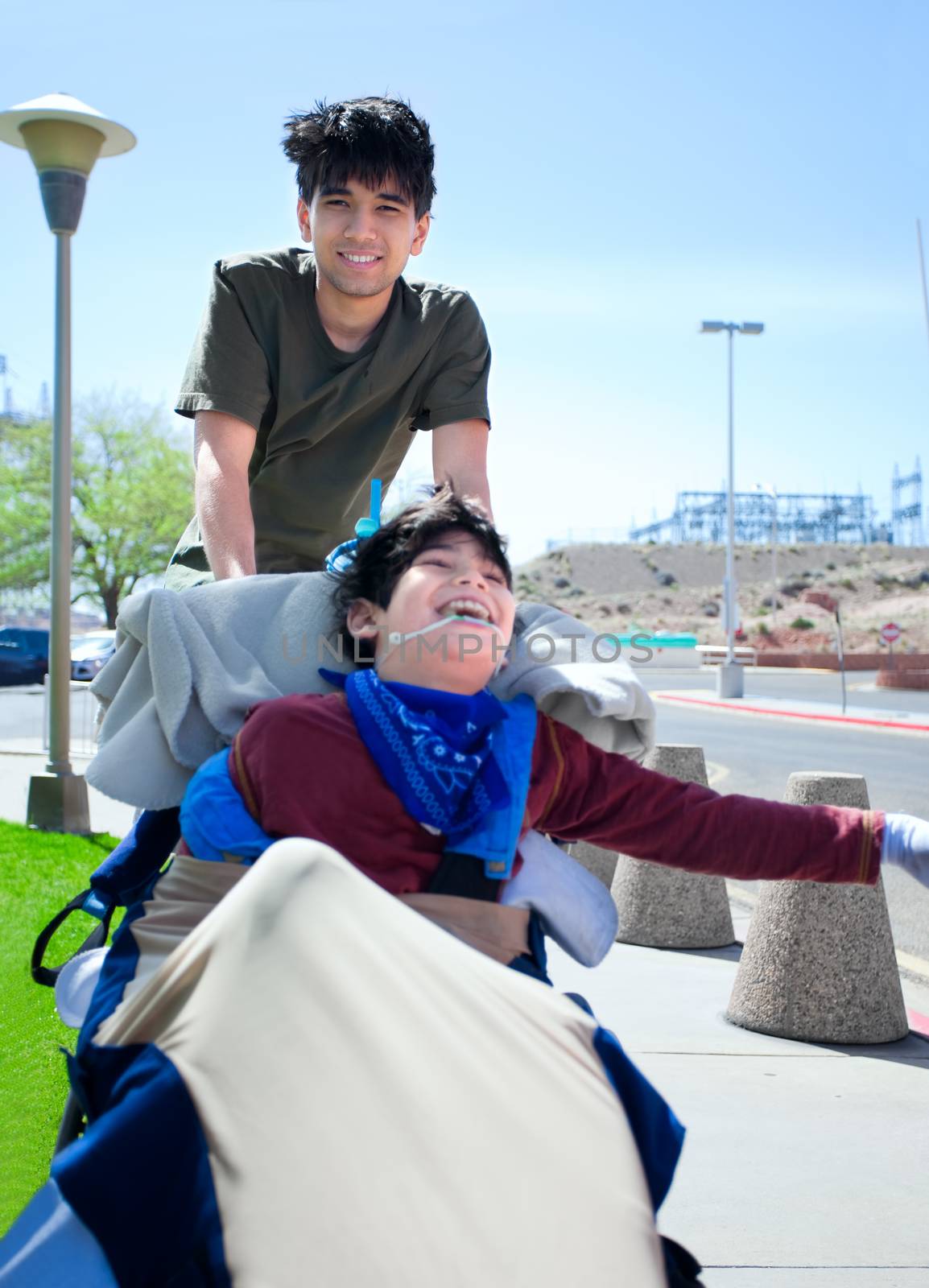 Big brother pushing happy disabled boy in wheelchair by jarenwicklund