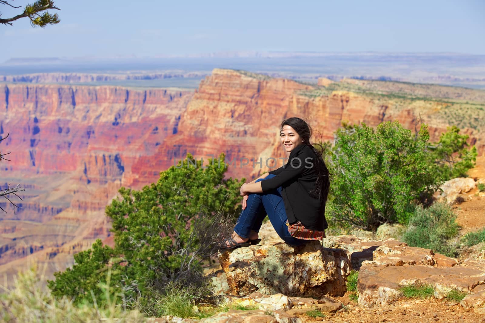 Biracial teen girl sitting along rock ledge at Grand Canyon by jarenwicklund