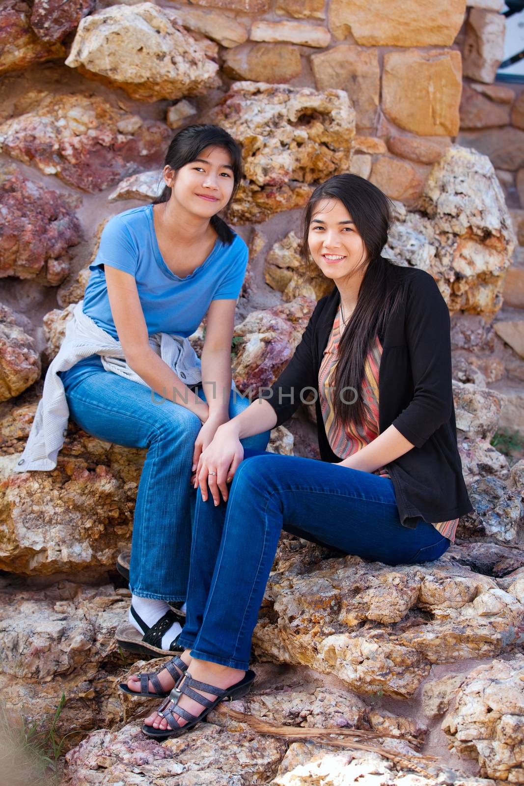 Two young teen girls sitting together on rocky stone seats by jarenwicklund