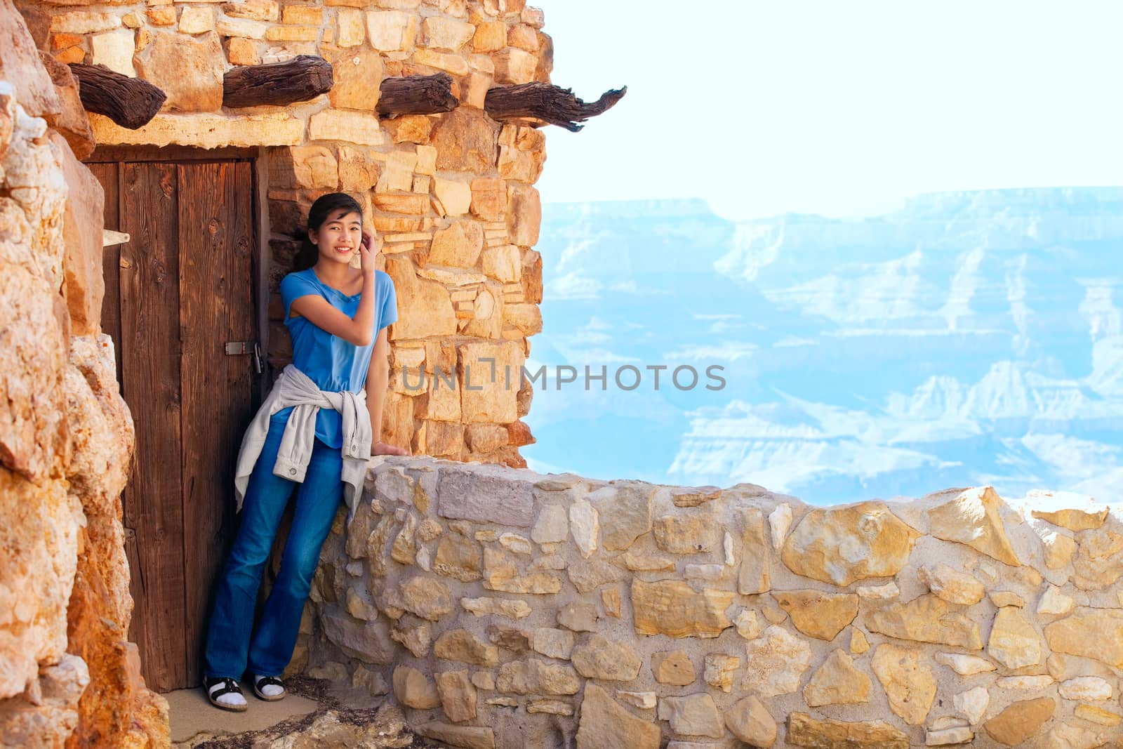 Biracial teen girl relaxing, leaning against rock wall overlooking Grand Canyon, next to doorway