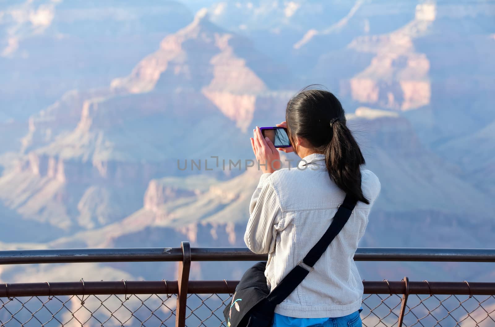 Young teen girl with pony tail standing at railing taking pictures at Grand Canyon, Arizona