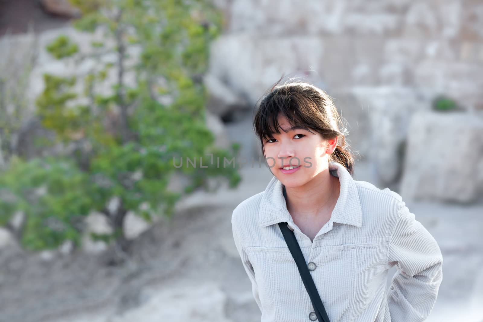 Young teen girl outdoors, smiling and looking at camera, rock wall in background