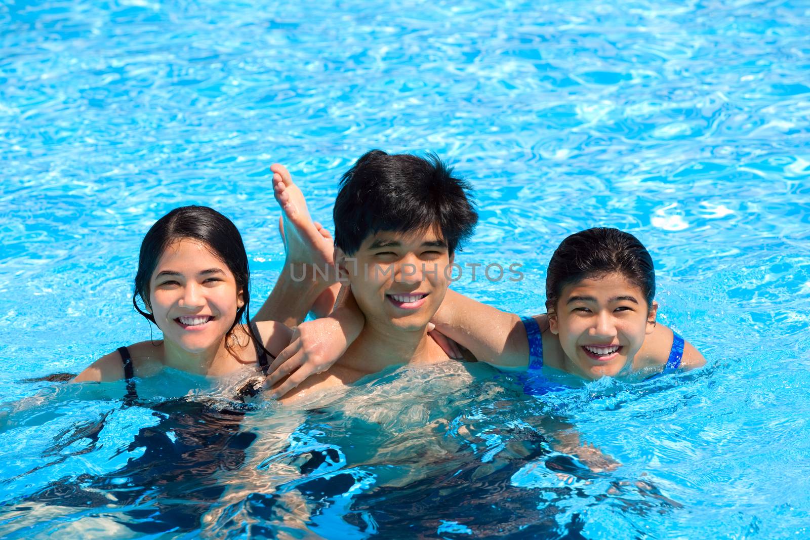 Three teen siblings smiling together in pool  by jarenwicklund