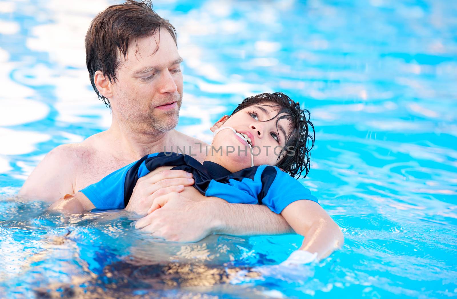 Father swimming in pool with disabled child by jarenwicklund