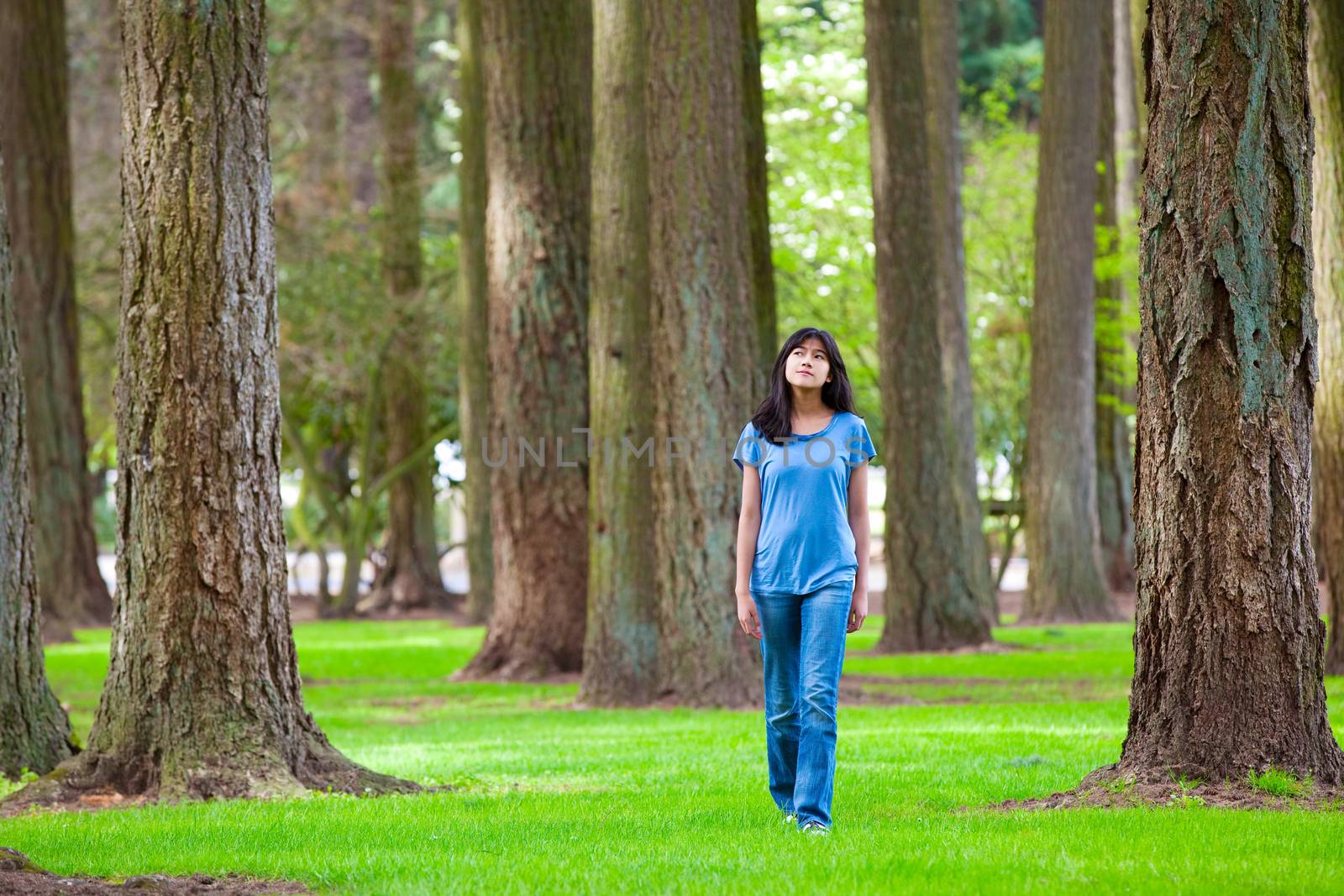 Young teen biracial girl walking under tall trees by jarenwicklund